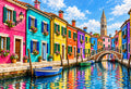Burano Houses Along the Canal — brightly painted Burano houses along a canal with moored boats, a small bridge and a leaning bell tower