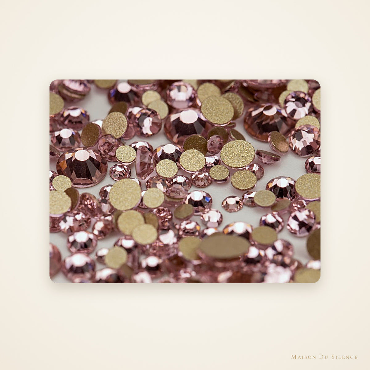 Close-up of Rose Lumière pink SS10 faceted flatback glass rhinestones on an ivory background